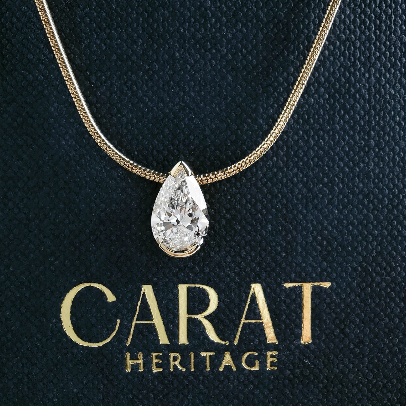 Pear diamond necklace on a dark background with 'Carat Heritage' branding.