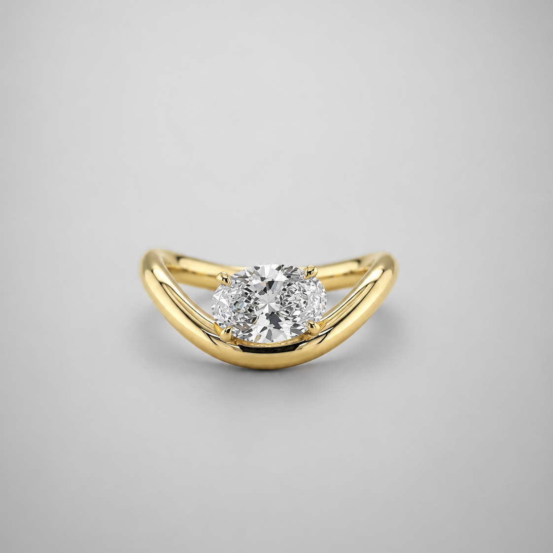 A yellow gold ring with a curved, wave-like band and a round-cut diamond center stone, shown on a neutral gray background.