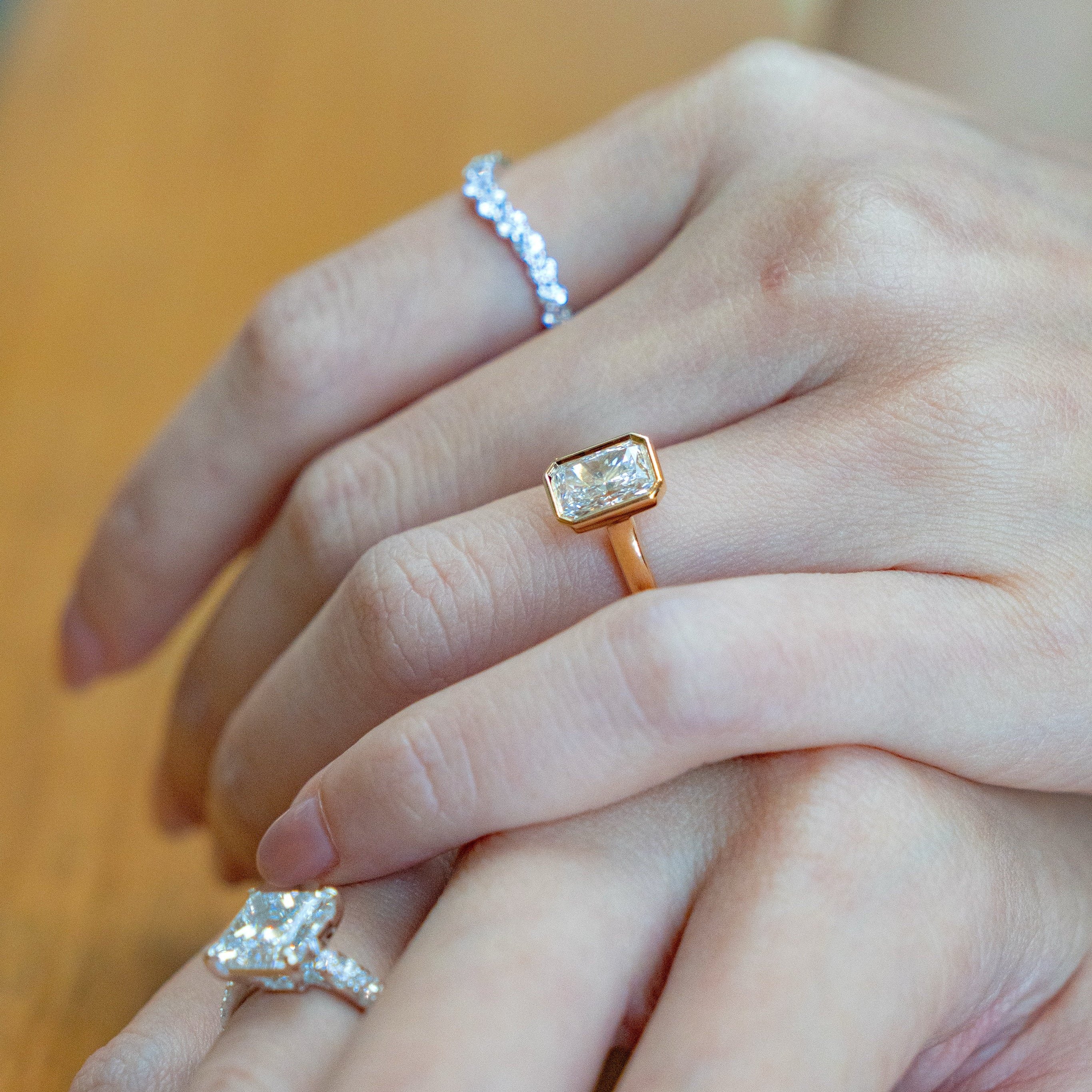 Hand wearing radiant ring, eternity ring and princess cut ring