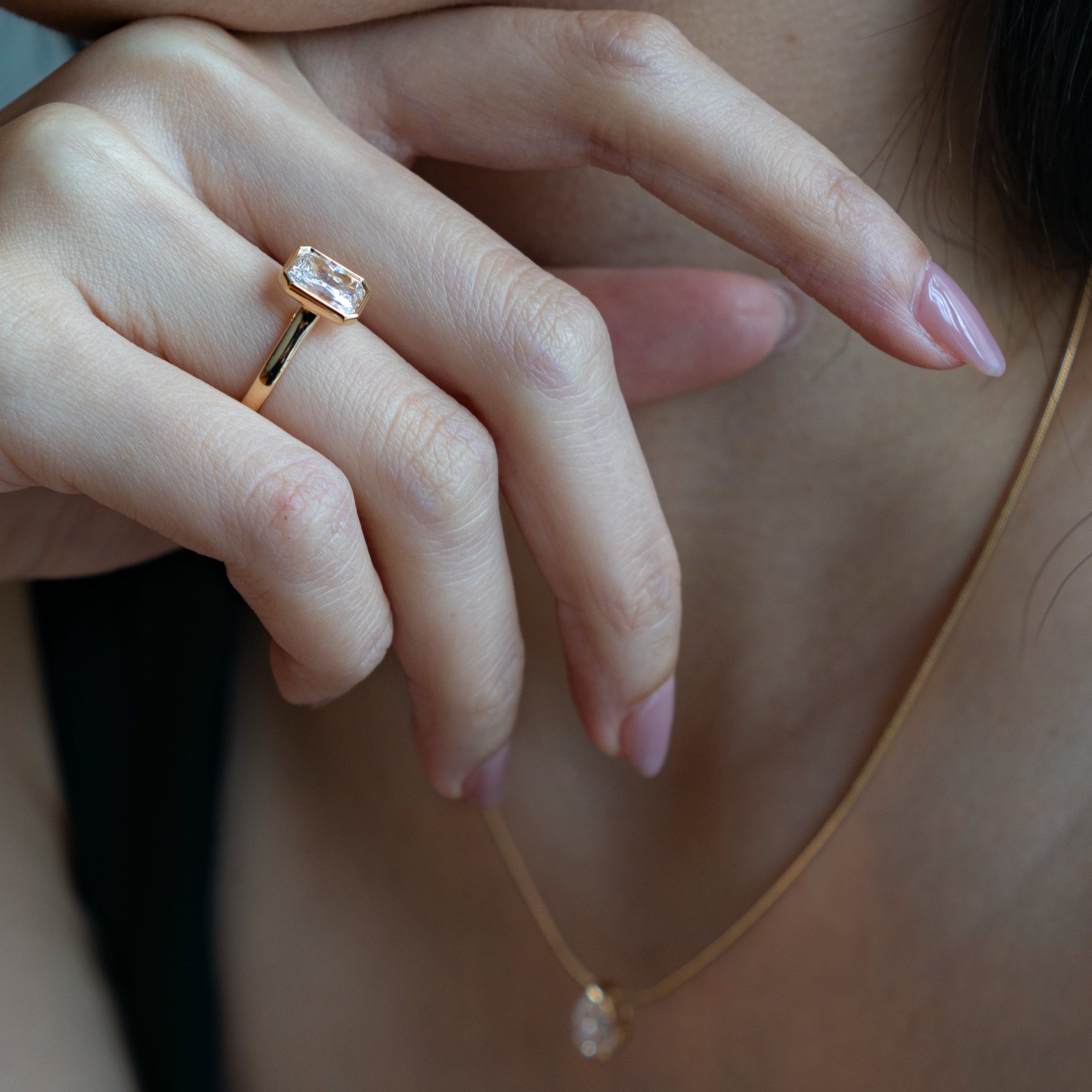 Close-up of a hand wearing a gold ring with a matching necklace featuring a pear diamond pendant.