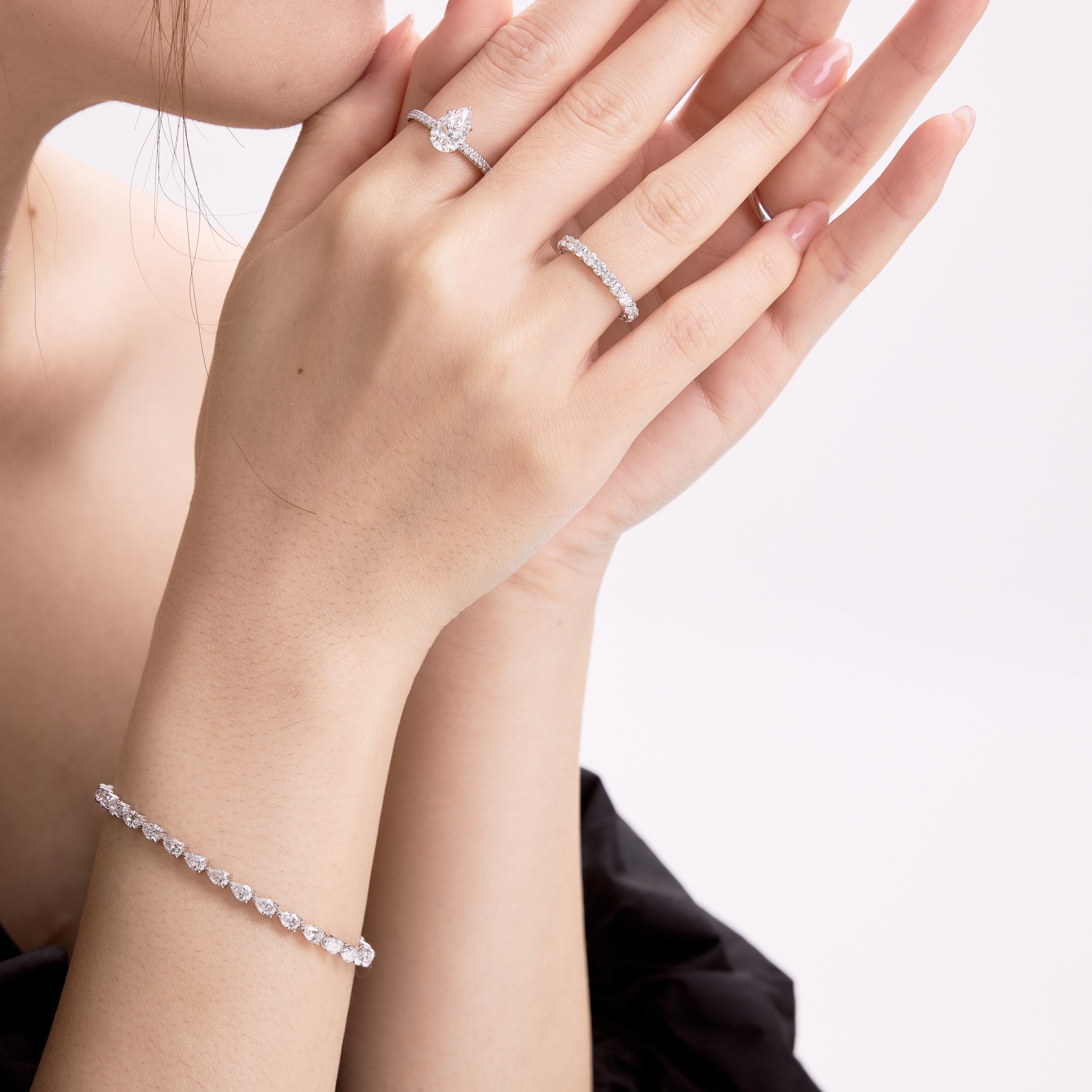 Close-up of a woman's hands wearing diamond rings and bracelet on a white background