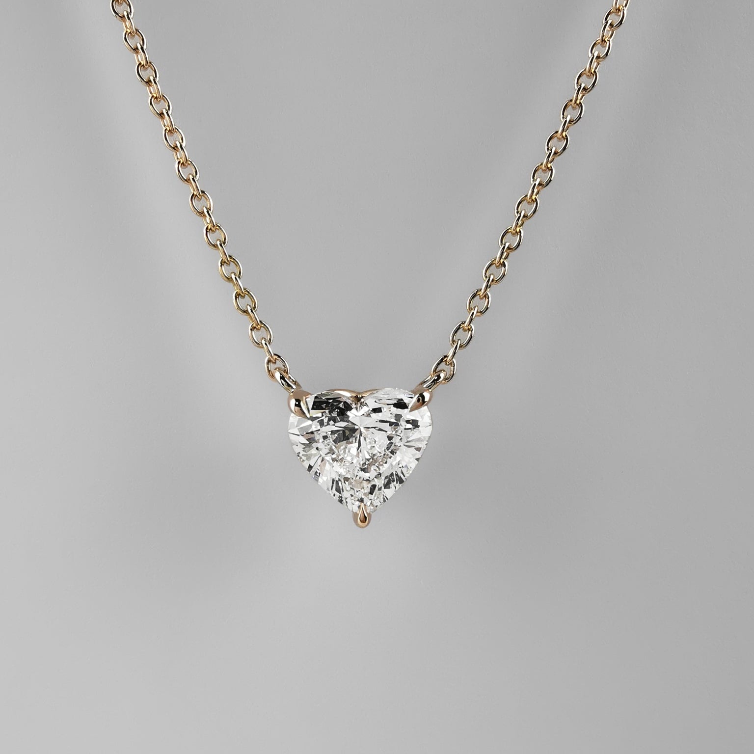 Heart-shaped diamond necklace on a gold chain against a gray background
